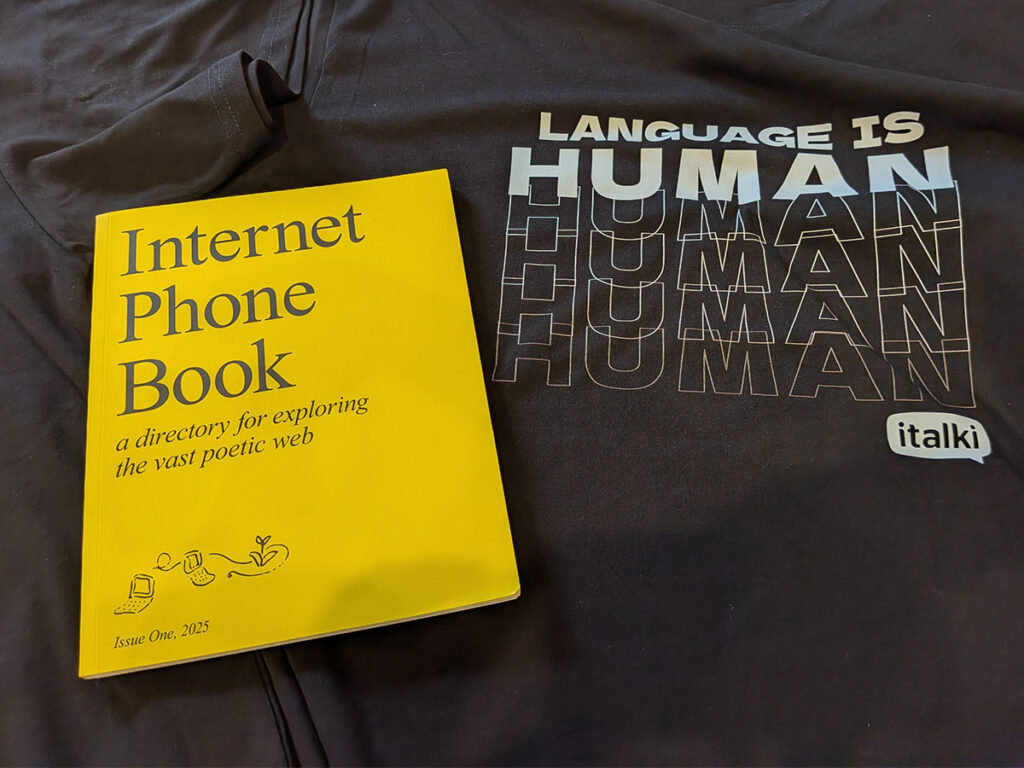 A bright yellow copy of the Internet Phone Book rests on a dark t-shirt featuring the repeating white text "LANGUAGE IS HUMAN."