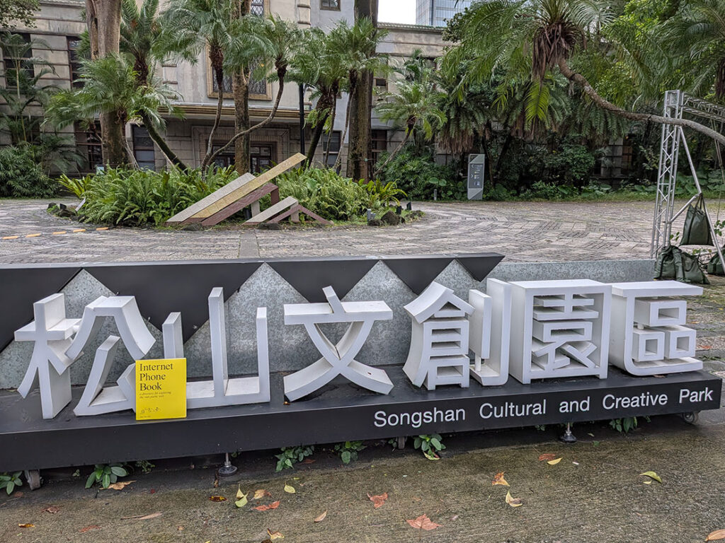 The yellow Internet Phone Book rests on a modern black-and-white sign for the Songshan Cultural and Creative Park in Taipei